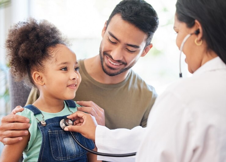 Pediatra examinando uma menina pequena com um estetoscópio, enquanto o pai da criança a observa com um sorriso