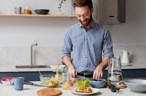 Rapaz em sua cozinha, preparando uma salada, viando uma alimentação saudável para homens