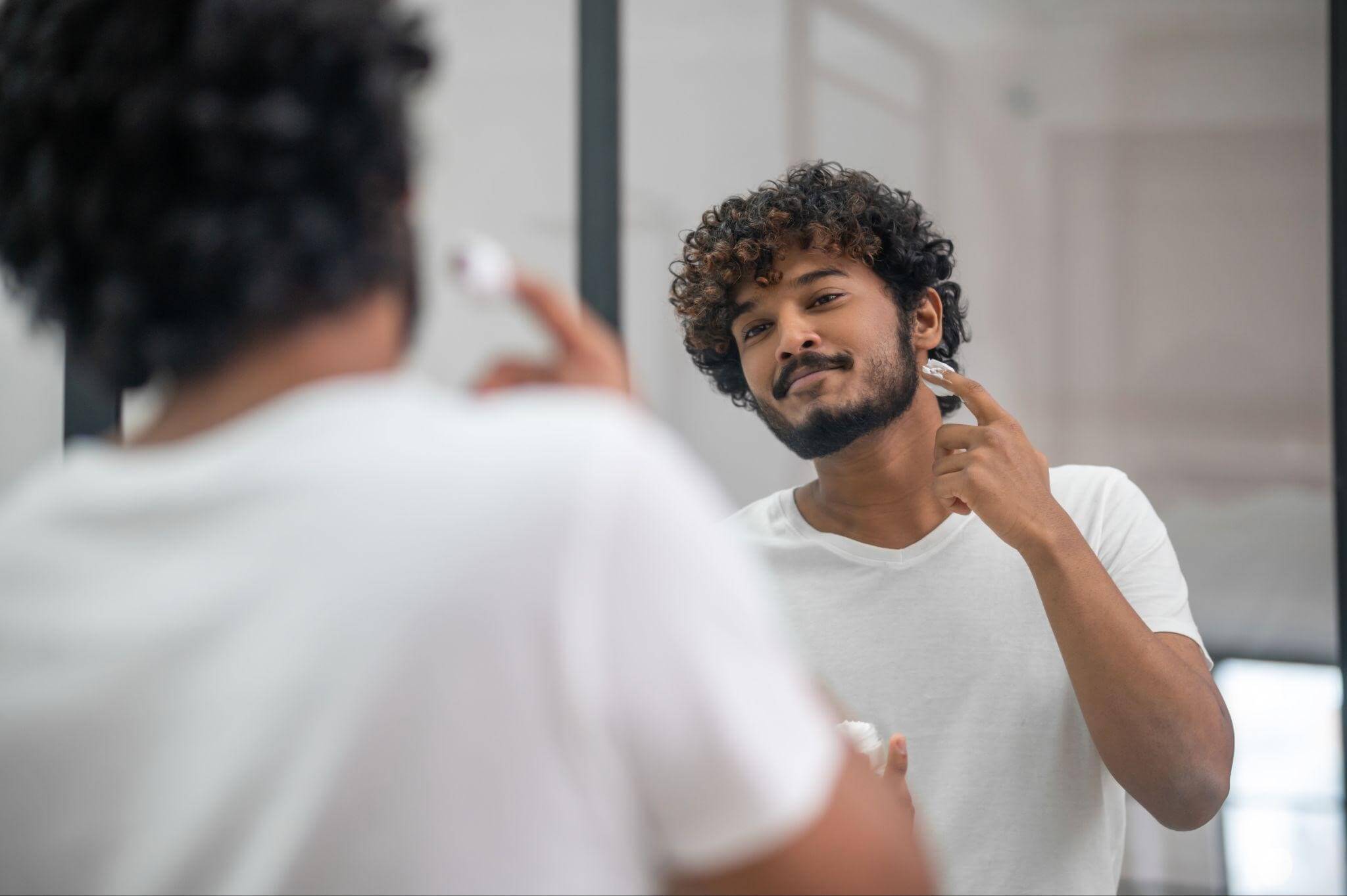 Homem em frente ao espelho, mantendo seu cuidados diários para manter sua barba saudável.